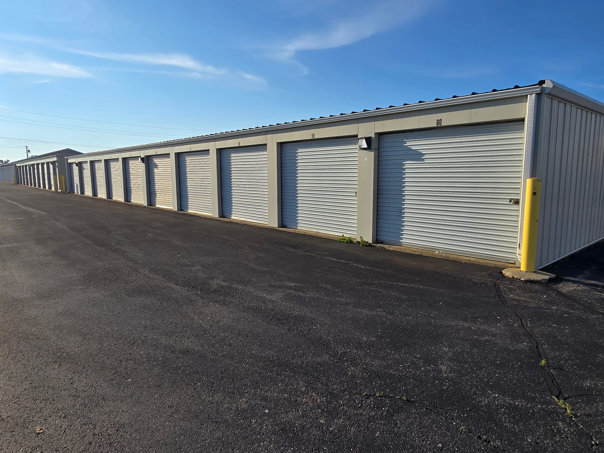 Row of clean drive-up storage units with roll-up doors under a blue sky at Evergreen Mini Storages