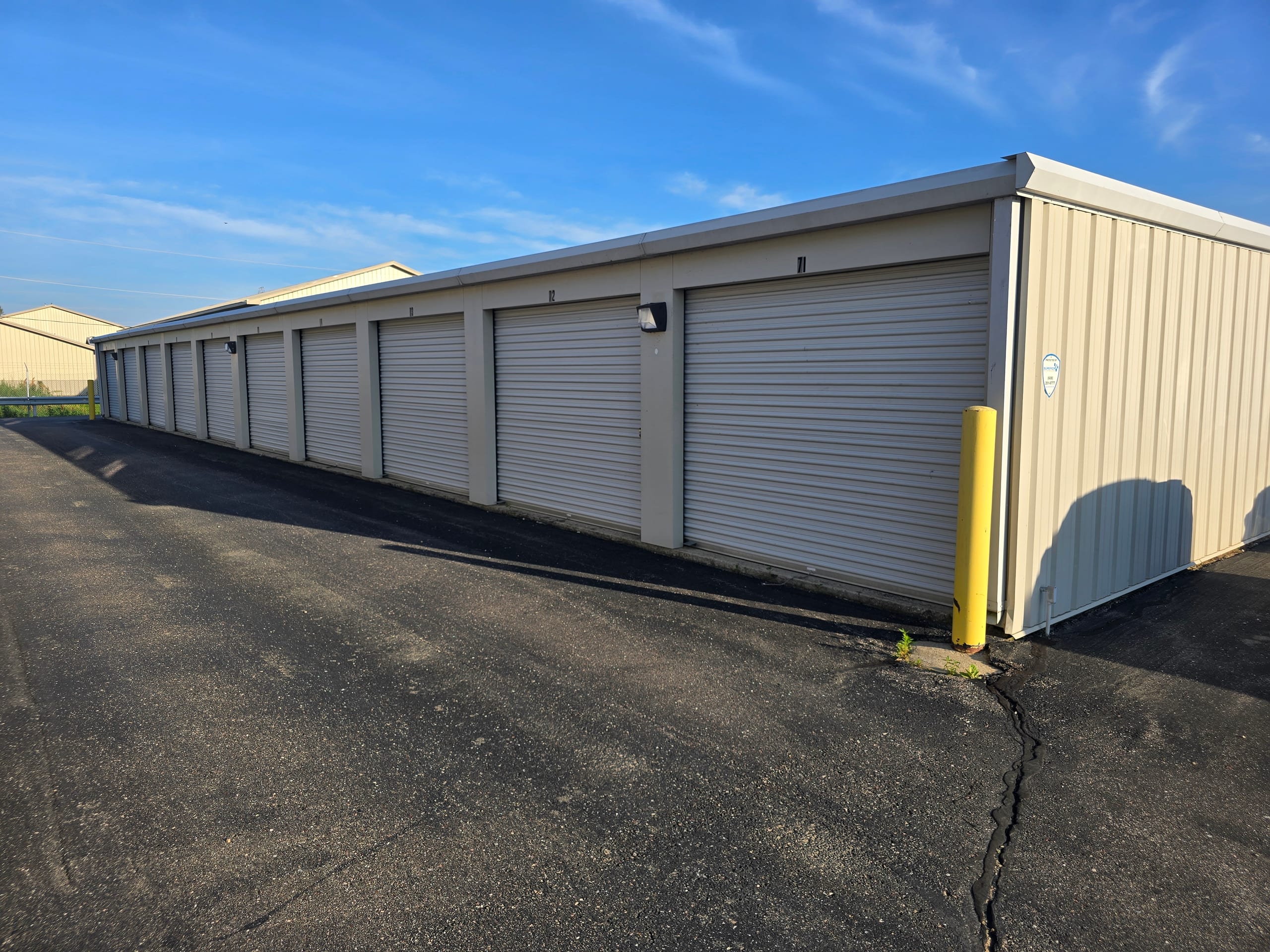 Long row of drive-up storage units with tan doors under a clear blue sky